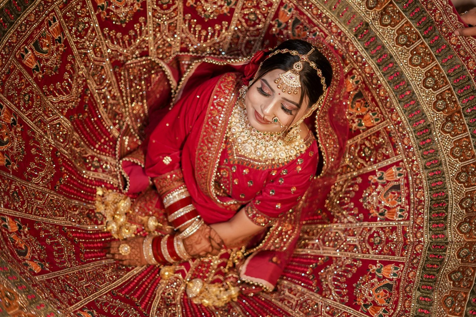 Overhead shot of a traditional Indian bride in a vibrant red lehenga adorned with intricate embroidery, capturing her calm and beauty.